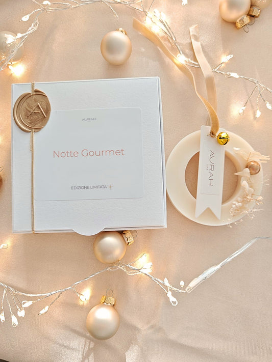 Ghirlandina Noël Aurah Lab in cera di oliva Notte Gourmet, accanto al packaging bianco con sigillo dorato, decorata con botaniche e nastro velluto oro, su sfondo natalizio luminoso.