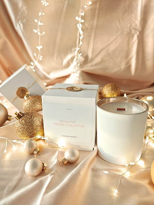Candela Aurah Lab “Notte Gourmet” in barattolo bianco accanto alla sua scatola con sigillo in cera, fotografata su un set dorato con luci calde e dettagli natalizi