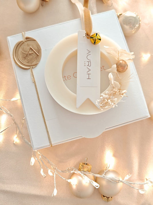 Ghirlandina Noël Aurah Lab in cera di oliva Notte Gourmet, appoggiata sul packaging bianco con botaniche e nastro velluto oro, in ambientazione natalizia luminosa.