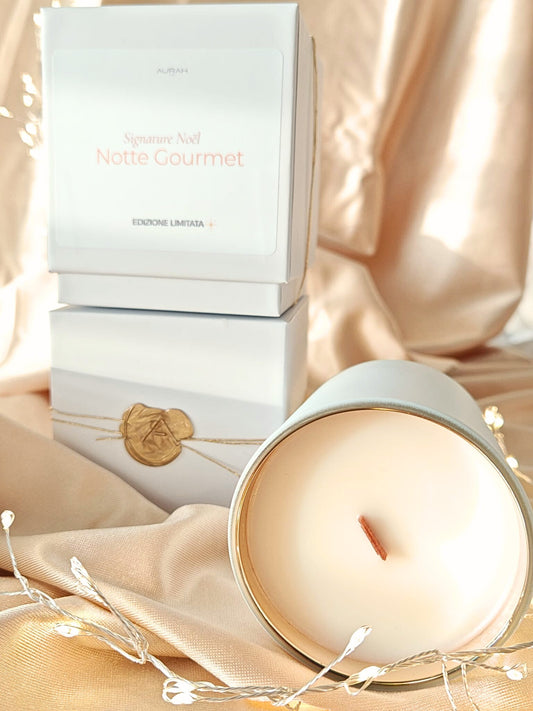 Candela Aurah Lab “Notte Gourmet” in barattolo bianco accanto alla sua scatola con sigillo in cera, fotografata su un set dorato con luci calde e dettagli natalizi.